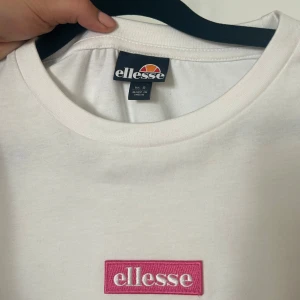 Vit t-shirt från Ellesse med rosa logga - Aldrig använd, endast testad! Vit t-shirt från Ellesse med klassisk passform och rund hals. På bröstet sitter en rosa broderad Ellesse-logga. Väldigt bekväm! 