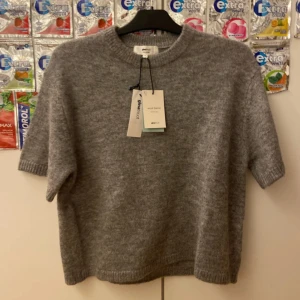 Grå stickad tröja från Gina Tricot - Mysig grå stickad tröja från Gina Tricot i ullblandning. Tröjan har korta ärmar, rund halsringning och en loose fit som ger en chill vibe. Perfekt att styla med jeans eller kjol för en enkel men snygg look.