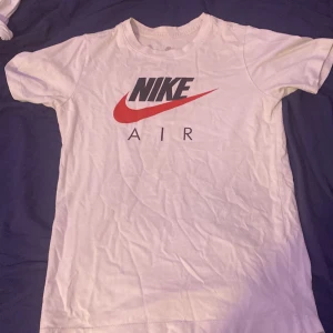 Vit Nike Air t-shirt med tryck - Vit t-shirt från Nike med klassiskt Air-tryck på bröstet i svart och rött. T-shirten har rund hals, korta ärmar och är gjord i mjuk bomull. Perfekt för dig som gillar sportig och clean stil.