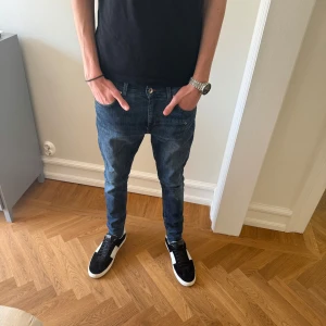 Blå jeans från Tiger of Sweden - Säljer ett par klassiska blå jeans från Tiger of Sweden. Jeansen har en slim passform med raka ben och snygga detaljer som kontrastsömmar och femficksdesign. Tillverkade i mjukt denimtyg som sitter skönt hela dagen.