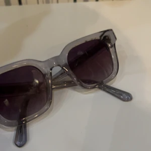 Grå transparenta solglasögon Chimi - Snygga solglasögon från Chimi med transparent grå båge och mörka glas. Modellen har en fyrkantig form som ger en cool vibe och passar till många stilar. Perfekta för soliga dagar när du vill sticka ut lite extra.
