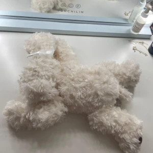 Ett jättegosigt hund gosedjur  - Bilderna visar ett mjukdjur från Bukowski, en söt och fluffig vit hund med långa öron och en rosett på huvudet. Den har mjuka tassar med bruna prickar och är perfekt som gosedjur eller present. Passar både unga och vuxna som gillar mysiga och charmiga mjukdjur. Den är knappt använd. 