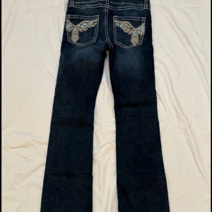 Mörkblå jeans med broderade fickor - Snygga mörkblå jeans med unika broderade detaljer i guld och blått på bakfickorna. Jeansen har klassisk passform och raka ben, perfekta för dig som vill sticka ut lite extra. Materialet är slitstarkt jeans och de har tydliga kontrastsömmar. dom har använt ett par fåtal gånger💞💞 pris kan såklart diskuteras vid snabbt köp!!