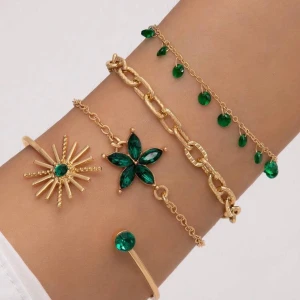 Guldarmband med gröna stenar - Fyra trendiga guldarmband med gröna stenar i olika former. Ett armband har en blomformad dekoration, ett har solstråle-design, ett är kedja med gröna droppar och ett är öppet med en grön sten i varje ände. Perfekt för att mixa och matcha.