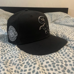 Svart White Sox keps från New Era - Snygg svart keps från New Era med White Sox-logga broderad framtill i vitt och silver. Kepsen har platt skärm och broderad detalj på sidan med årtalet 1917. Perfekt för dig som gillar sportig streetstyle. 🔴Helt ny, endast tagit bort lappar och sånt 🔴