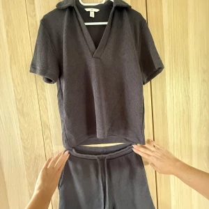 Mörkgrå stickad set H&M - Mörkgrå stickad set från H&M med en piké med krage och djup v-ringning. Tröjan har korta ärmar och en avslappnad passform, perfekt för chill dagar. Materialet är mjukt och lite grovstickat vilket ger en skön känsla. 