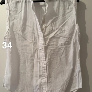 Vit ärmlös skjorta med knappar - Klassisk vit skjorta i bomull med knappar framtill och en bröstficka. Skjortan är ärmlös och har en rak passform, perfekt för varma dagar eller lager på lager. Enkel och stilren design som passar till det mesta.🌸Fint använt skick.  Storlek 34