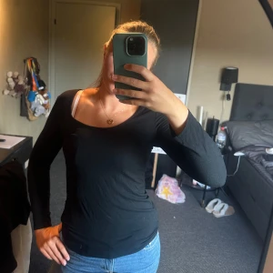 Svart långärmad topp med snörning - Svart långärmad topp med snygg snörning i ryggen och bred, rundad urringning fram. Tight passform som sitter snyggt på kroppen. Perfekt till jeans för en stilren look.