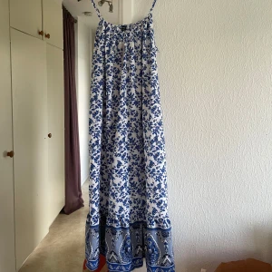  Långklänning från Emery Rose - Superfin långklänning från Emery Rose med smala axelband och lös passform. Prislapp kvar. Klänningen är vit med blått blommönster och har en dekorativ bård längst ner. Perfekt för sommardagar och enkel att styla med sandaler eller sneakers. 