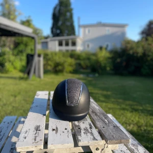 Svart ridhjälm USG med glitterdetalj - Snygg svart ridhjälm från USG i storlek 52-54. Hjälmen har en glittrig detalj framtill och silverfärgad kant. Den är väldigt bra skick och går att justera i storlek . Säljer då passformen inte riktigt passar😊hör gärna av er om ni har frågor priset kan diskuteras 😀