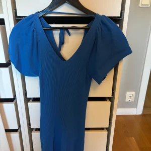 Blå ribbad klänning från ONLY - Supersnygg blå ribbad klänning från ONLY med puffiga korta ärmar och v-ringning. Klänningen har en figurnära passform och knytning i nacken. 