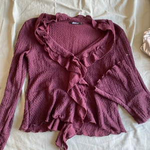 Vinröd blus Gina Tricot - Supersöt vinröd omlottkofta från Gina Tricot med volangdetaljer längs krage och framkant. Långärmad och i ett mjukt, strukturerat material. Aldrig använd.