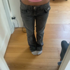 Lågmidjade  jeans - Säljer ett par mörkgrå jeans med bootcut passform och låg midja. Jeansen har klassiska fem fickor och snygg tvättad look. Perfekta för dig som gillar en avslappnad men ändå trendig stil. Storlek 158 men passar som xs       Midjemått: 33cm Innerbenslängd: 72 cm Hela jeansen: 93cm