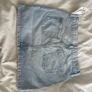 Ljusblå jeanskjol med slitna detaljer - Trendig ljusblå jeanskjol med råa kanter och slitna detaljer. Kjolen har klassiska fickor fram och bak, bälteshällor och knappstängning. Perfekt för dig som gillar en avslappnad och cool stil. Ordinarie pris 250 men säljer för 200 aldrig använd prislapp kvar 