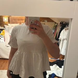 Vit blus med volang från SHEIN - Supersöt vit blus från SHEIN med diskreta ränder och volang nedtill. Blusen har korta ärmar med liten volangkant och en lös, flowy passform. Perfekt för dig som gillar en romantisk och luftig stil. Toppen är köpt från Sellpy och har aldrig använts hos mig. Ganska liten i storlek så passar nog en xs bättre💞