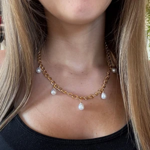 Pärlhalsband Guld  - Snyggt halsband med chunky guldfärgad kedja och fem droppformade vita pärlor som hänger längs kedjan. Perfekt statement-piece som lyfter vilken outfit som helst. Kedjan har en modern och trendig look med klassiska pärldetaljer.