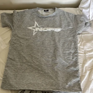 Grå t-shirt med NOFS-tryck - Snygg gråmelerad t-shirt från NOFS med stort vitt stjärntryck och logga på bröstet. Klassisk rund halsringning och korta ärmar. Perfekt för en chill och avslappnad stil. Materialet känns mjukt och skönt mot huden.
