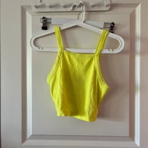 Gul croppad linnetopp - Snygg croppad linnetopp i en riktigt poppig gul färg. Toppen har breda axelband och är tillverkad i ett mjukt, ribbat bomullstyg som sitter skönt mot kroppen. Perfekt för varma dagar när du vill sticka ut lite extra.