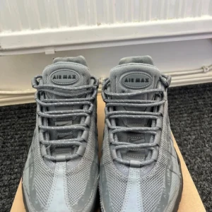 Nike Air Max 95 grå sneakers - Nike Air Max 95 sneakers i helgrå färg med mesh och syntetpaneler. Skorna har tydlig Air Max-dämpning i sulan, snörning framtill och diskreta Air Max-loggor längs sidan. Swoosh-logga på hälen och klassisk rund tå. Perfekt för dig som gillar sportig och clean stil.