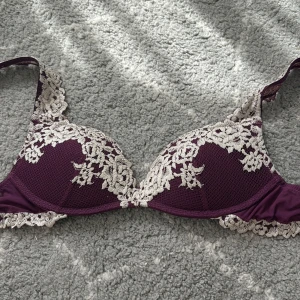 Lila spets-bh med blommig detalj - Superfin lila bh med vita blommiga spetsdetaljer och vadderade kupor. Snygg meshstruktur på kuporna och spets längs kanterna ger en romantisk vibe. Perfekt för dig som gillar detaljer och vill ha något extra under tröjan. Den är från intimissimi!