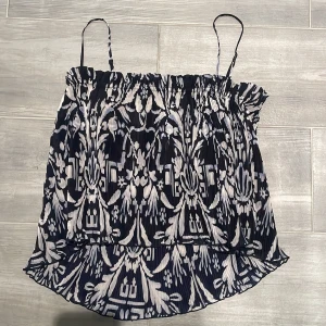 Sommarig topp  - Säljer en blåvit plisserad linnetopp med tunna axelband och ett snyggt grafiskt mönster. Toppen har en luftig passform och är perfekt för varma dagar. Den har en lätt glansig yta och är superenkel att styla till jeans eller kjol. 