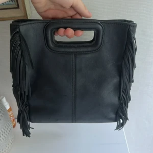 Svart axelväska från maje - Snygg svart axelväska i skinn från Moie med fransar längs sidorna och både handtag och lång axelrem. Väskan har en stilren, fyrkantig form och diskret logga framtill. Perfekt för dig som vill ha en cool och trendig accessoar. Orginal pris vid 4000!💕💕