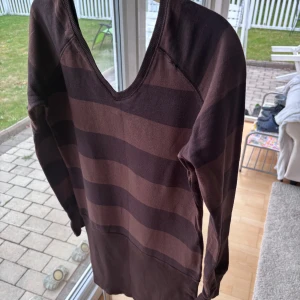 Brunrandig tröja - Mysig långärmad tröja med breda bruna och mörkbruna ränder. Tröjan har en djup v-ringning och ribbade muddar vid ärmsluten. 