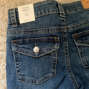 Y2K low bootcut jeans från Gina Tricot - Snygga blå bootcut jeans med låg midja från Gina Tricot. Klassisk femficksmodell med coola fickdetaljer bak och kontrastsömmar. Jeansen har en Y2K-vibe och är tillverkade i bomullsmix för en skön passform. aldrig andvända då de tyvärr är lite stora för mig💓 alla lappar kvar