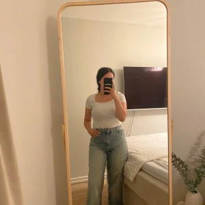 Blåa wide high waist jeans - Säljer ett par ljusblå jeans med hög midja och breda ben. Jeansen har klassisk femficksdesign, bälteshällor och stängs med dragkedja och knapp. Perfekta för dig som gillar en loose och avslappnad stil.