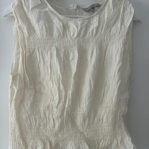 Vit ärmlös blus med rynkade detaljer - Säljer en vit ärmlös blus med rynkade partier och rund halsringning. Mycket bra skick💕