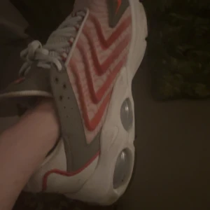 Nike Air max TW stl 44,5 använda 2ggr - Säljer ett par Nike Air sneakers med vit bas, röda och grå detaljer samt tydliga vågmönster på sidorna. Skorna har snörning och en tjock, vit sula med synliga luftbubblor. Perfekta för dig som gillar sportig stil.