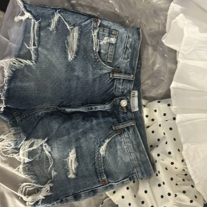   jeansshorts Zara  - Säljer ett par blå jeansshorts från  Zara med slitna detaljer och fransar nertill. Klassisk femficksmodell med knapp och dragkedja framtill. Perfekta för sommaren och ger en cool, avslappnad look. Skriv vid intresse