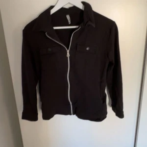 Svart jacka med dragkedja - Svart jacka med vit dragkedja och krage. Två bröstfickor med knappar framtill. Långärmad och enkel design, passar till många olika stilar. Den är köpt på Zalando men sälj inte längre storlek är 152 säljer då den tyvärr är för liten 