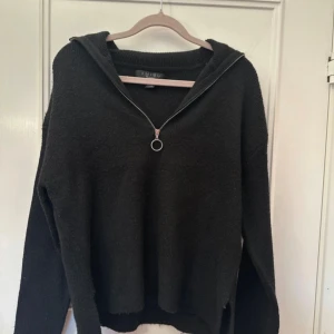 Svart stickad tröja med dragkedja från Amisu - Svart stickad tröja från Amisu/New Yorker med lång ärm och hög krage. Tröjan har en snygg silverfärgad dragkedja framtill som kan öppnas hela vägen ner till bröstet. Perfekt för lager-på-lager och enkel att styla.