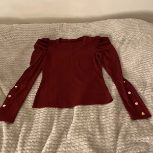 Vinröd långärmad topp med puffärmar och guldknappar - Oanvända! Vinröd långärmad topp med puffärmar och dekorativa guldknappar längs ärmsluten. Toppen har en rund halsringning . Storlek M men passar mig som har xs/S . Något lite lite stor men kan fortfarande ha den utan att den ser för stor ut💗okänt märke? 