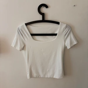 Vit croppad topp med fyrkantig ringning - Säljer en stilren vit croppad topp med fyrkantig ringning och korta ärmar. Man kan använda uringningen både fram och bak! Aldrig använd😊