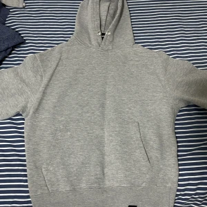 Grå hoodie från Pull&Bear - Säljer en enkel och stilren grå hoodie från Pull&Bear. Tröjan har huva med dragsko och en stor magficka framtill. Perfekt för en avslappnad och bekväm stil. Klassisk passform och mjukt material.