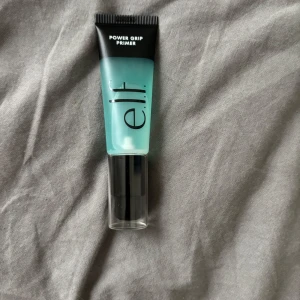 e.l.f. Power Grip Primer - Säljer en e.l.f. Power Grip Primer i en genomskinlig tub med svart pump och lock. Primern är blågrön och ger en jämn bas för smink. Perfekt för att få sminket att sitta längre och ge en fräsch finish.