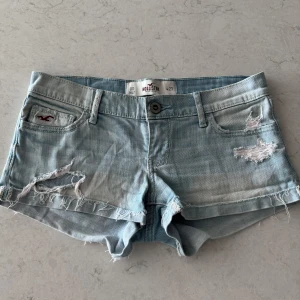 Ljusblå jeansshorts från Hollister - Säljer ett par ljusblå lågmidjade jeansshorts från Hollister med slitna detaljer. Shortsen har en fin ljusblå färg som passar till många outfits. Fickorna har detaljer och hollistermärket syns på framsidan. Längd i midjan 37 cm så snarare stl w25. Säljer pga av att de tyvärr var för stora för mig.