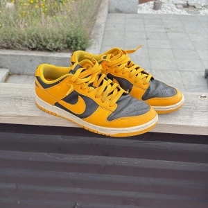 Nike Dunk sneakers i gult och svart - Säljer ett par Nike Dunk sneakers i gult och svart med klassisk låg modell. Skorna har snörning, vit mellansula och tydlig Nike-logga på sidan och hälen. Perfekta för dig som gillar färgstarka och sportiga sneakers nu till sommaren!