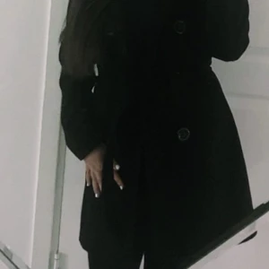 Svart kappa med knappar och bälte - Säljer en svart kappa med knappar framtill och bälte i midjan. Klassisk och stilren modell som passar perfekt till jeans eller kostymbyxor. Långärmad och med en figursydd form. Nästan helt ny. Storlek M men funkar som S 