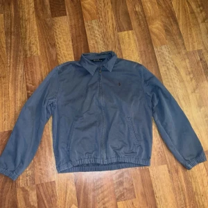  Polo Ralph Lauren - Säljer en vintage navy jacka från Polo Ralph Lauren med dragkedja framtill och krage. Jackan har långa ärmar, två sidofickor och elastisk midja samt ärmslut. Perfekt för vår och höst. Stolen M