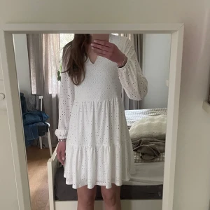 Vit långärmad klänning med broderade detaljer från Vila - Superfin vit klänning från Vila med v-ringning och lång ärm. Klänningen har broderade spetsdetaljer och är perfekt till sommaren. Passar bra till student eller examen. Är öppen för prisförslag 
