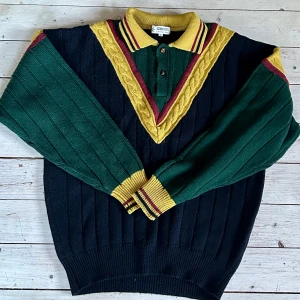 Björn Borg Rohdi Heintz 80-tal  - Säljer en unik stickad pikétröja från Björn Borg i grönt och mörkblått med gula och vinröda detaljer. Design Rohdi Heintz. Tröjan har lång ärm, ribbade muddar och klassisk krage med knappar. Perfekt för dig som gillar retrostil. Storlek XL. 