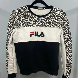 Leopardmönstrad sweatshirt från FILA - Cool sweatshirt från FILA med leopardmönster på axlar och ärmar, svart nederdel och vit bröstpanel med stor logga framtill. Rund halsringning och långa ärmar. Perfekt statement-plagg för dig som gillar att sticka ut.