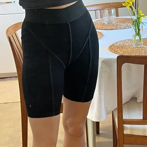 Svarta cykelshorts från NA-KD x Hanna Schönberg - Svarta cykelshorts med hög midja från NA-KD x Hanna Schönberg. De har bred resår i midjan och synliga sömmar. Materialet är stretchigt och bekvämt.