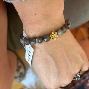 Grått armband med guldfärgad detalj - Stilrent armband med runda grå pärlor och en dekorativ guldfärgad detalj i mitten. Perfekt accessoar för att lyfta din outfit med en elegant touch.