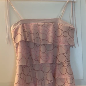 Ljusrosa volangtopp med mönster från Topshop - Söt ljusrosa topp från Topshop med tunna axelband och volanger. Toppen har ett cirkelmönster i rosa och brunt och är perfekt för varma dagar. Axelbandslös känsla med flera lager volanger framtill.