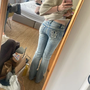Ljusblå bootcut jeans från Stars & Stripes - Säljer ett par ljusblå bootcut jeans från Stars & Stripes med snygga broderade detaljer på bakfickorna. Jeansen har låg midja och klassisk femficksdesign. Använda max 3 gånger
