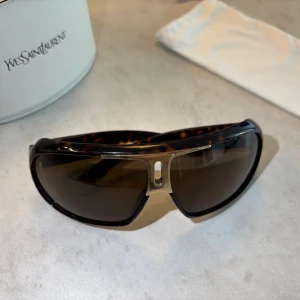Snygga Yves Saint Laurent solglasögon för sommarn! - Snygga Yves Saint Laurent Havana Brown full rim solglasögon, sturdy plastic frame, gold tone metal ware. Model: 2199/S, Made in Italy Använda men fortfarande i bra skick, kommer med fodral. Några små repor på linsen, liten skrapa längst ut på bågen, och på fodralet, visas på bild. Skriv om frågor, kan skicka bilder!